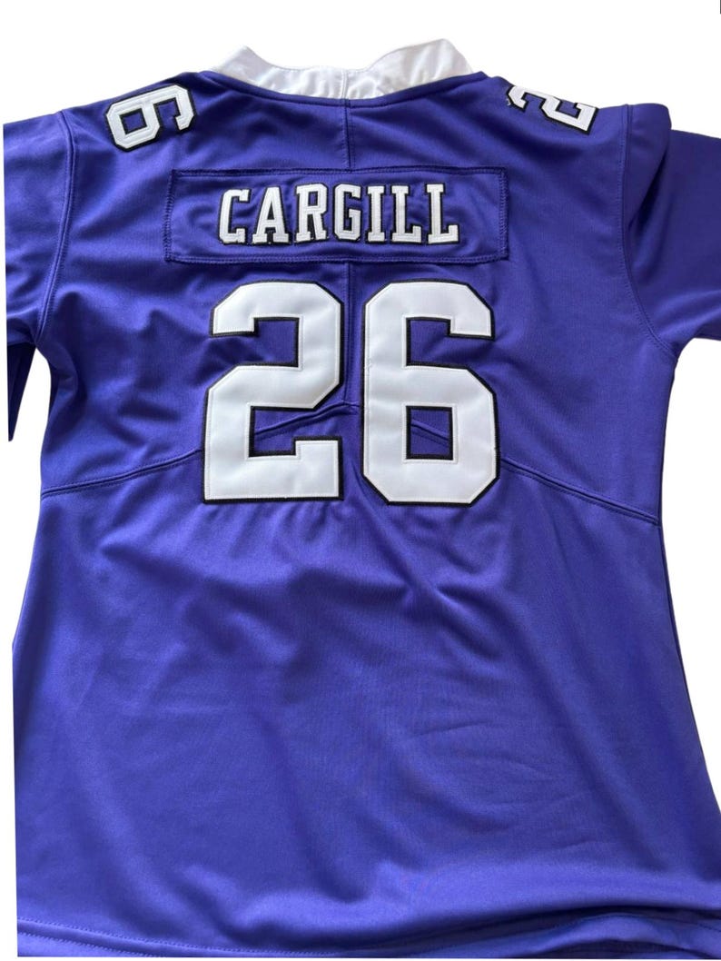 Puede incluir: Una camiseta de f&uacute;tbol morada con letras y n&uacute;meros blancos. El nombre "CARGILL" se muestra encima del n&uacute;mero "26" en la espalda. El n&uacute;mero "6" es visible en el hombro.