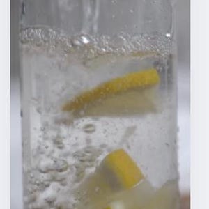 Op de afbeelding: Een helder glas gevuld met bruisend water en citroenpartjes. De citroenpartjes, met gele schil, zijn gedeeltelijk ondergedompeld in de bruisende vloeistof. Het glas is bedekt met condensatie.