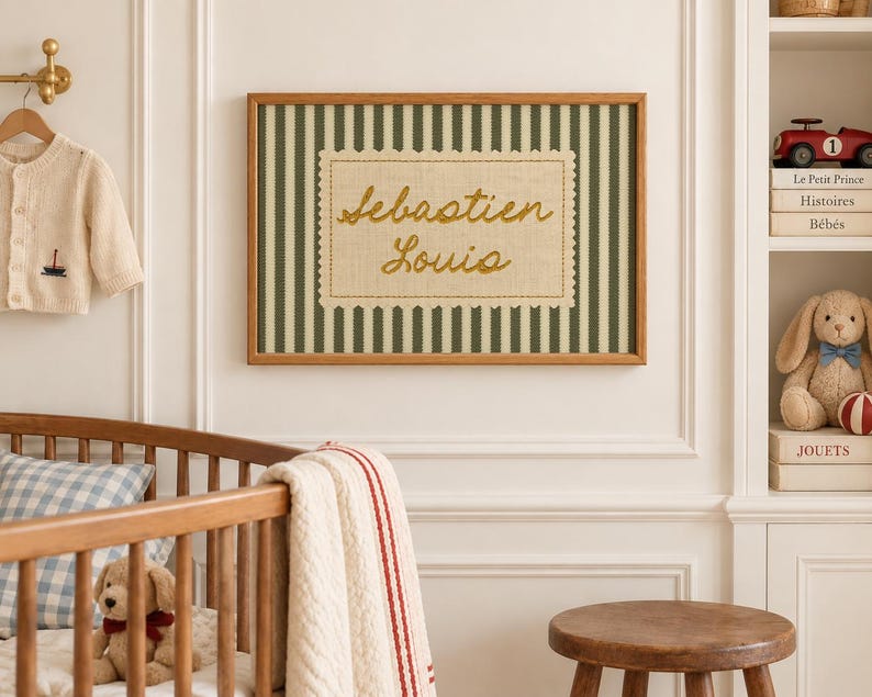 May include: A rectangular wall art piece in a wooden frame featuring a dark green and white vertical striped background. Centered is a beige fabric patch with scalloped edges, embroidered with the name Sebastien Louis in gold thread.