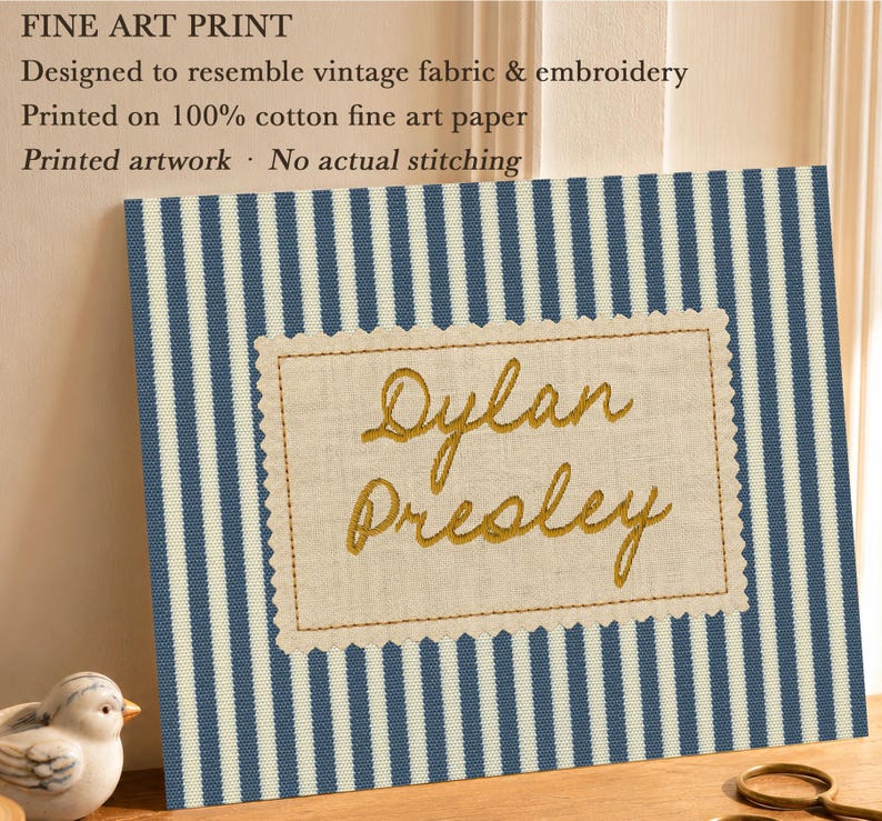 May include: A fine art print featuring a blue and white vertical striped pattern with a central rectangular beige patch. The patch has a scalloped edge and displays the name Dylan Presley in gold script. Text on the print reads: FINE ART PRINT, Designed to resemble vintage fabric & embroidery, Printed on 100% cotton fine art paper, Printed artwork &middot; No actual stitching.