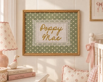 May include: A rectangular framed wall art piece featuring a sage green fabric background with a white polka dot pattern. Centered is a rectangular white fabric panel with lace trim, embroidered with the gold cursive text Poppy Mae.