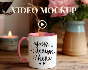 May include: A white coffee mug with a pink handle and rim being filled with coffee. The mug has the text "your design here" in black script. The image also includes a candle, flowers, and the text "VIDEO MOCKUP".