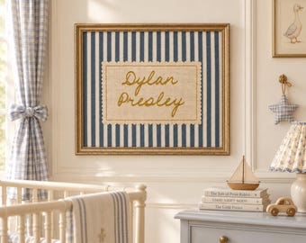 May include: A rectangular wall art piece in a gold frame featuring a navy blue and white vertical striped background. Centered is a cream-colored fabric patch with scalloped edges, embroidered with the name Dylan Presley in gold cursive script.