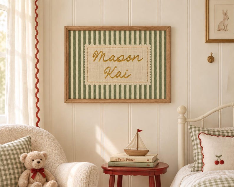 May include: A rectangular wall art piece in a wooden frame featuring a green and white vertical striped background. Centered is a beige fabric patch with a scalloped edge, embroidered with the name Mason Kai in gold cursive script.
