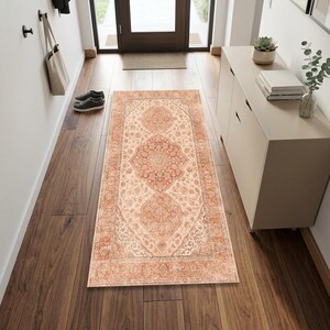 May include: A rectangular area rug featuring a central medallion design in shades of terracotta, cream, and muted gray. The rug displays an intricate floral and vine pattern with a wide decorative border, laid flat on a dark wood floor.