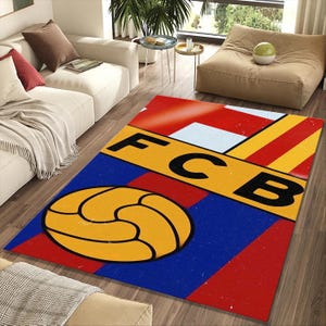 Op de afbeelding: Een rechthoekig vloerkleed met het FC Barcelona-logo. Het vloerkleed heeft een blauwe achtergrond met een gele en zwarte voetbalafbeelding. De letters "FCB" staan in zwart op een gele streep, met rode en witte strepen erboven.