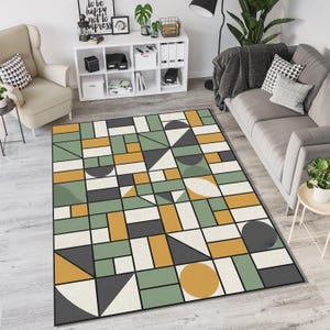 May include: Geometric patterned area rug featuring a modern design. The rug has a black border and a pattern of rectangles, squares, triangles, and circles in shades of green, yellow, gray, and white. The rug is placed in a living room setting.