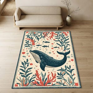 Op de afbeelding: Een rechthoekig vloerkleed met een centraal geplaatste donkerblauwe walvis op een crèmekleurige achtergrond. Het ontwerp bevat rood koraal, donkergroen zeewier en kleine vissilhouetten, omlijst door een donkerblauwe decoratieve rand.