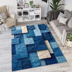 Könnte beinhalten: Ein rechteckiger Teppich mit einem 3D-geometrischen Design. Der Teppich zeigt ein Muster aus überlappenden Quadraten in Blau- und Beigetönen, wodurch ein strukturiertes Aussehen entsteht. Der Teppich liegt auf einem hellen Holzboden, geeignet für ein Wohnzimmer. Ca. 200 cm x 300 cm.