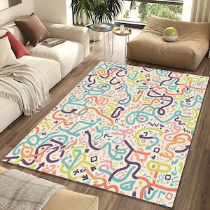 May include: A rectangular area rug with a cream background and a colorful abstract design. The design features looping lines, arrows, and geometric shapes in shades of orange, purple, teal, pink, and green.