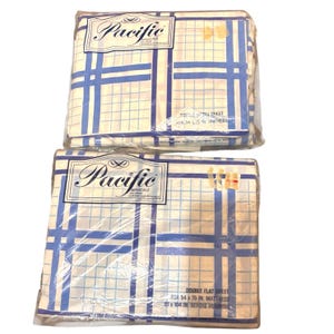 May include: Two packaged Pacific brand bed sheets. The sheets have a white background with a blue grid pattern. The packaging includes the text "DOUBLE FITTED SHEET FOR 54 x 75 IN. MATTRESS" and "DOUBLE FLAT SHEET FOR 54 x 75 IN. MATTRESS 81 x 104 IN. BEFORE HEMMING".