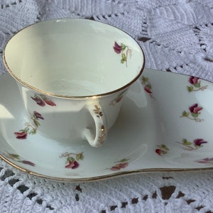 Peut inclure: Une tasse à thé et une soucoupe blanches avec un motif floral. La tasse a une bordure dorée et la soucoupe a un bord festonné.