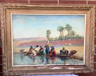 Puede incluir: Una pintura al óleo antigua en un marco de madera dorada. La obra representa una escena con figuras cerca del agua, palmeras y un fondo montañoso. La pintura tiene una firma en la esquina inferior derecha.