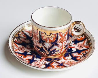 May include: A vintage teacup and saucer set. The cup and saucer feature a white background with intricate patterns in orange, blue, and gold. The cup has a gold handle and rim, and the saucer has a matching design. A classic addition to any tea set.