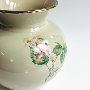 May include: A pale green ceramic vase with a gold rim. The vase has a floral design with pink and white flowers, green leaves, and small white polka dots. A decorative item for the home.
