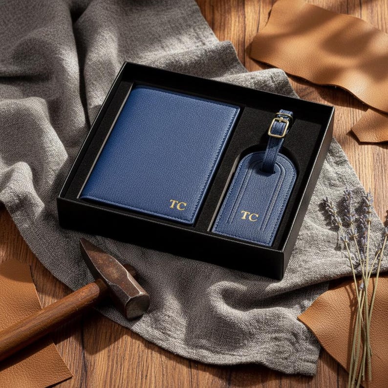 May include: A blue leather travel set in a black box, including a passport holder and luggage tag. Both items are embossed with the initials "TC" in gold. The set is presented on a gray cloth, with leather scraps and a hammer in the background.