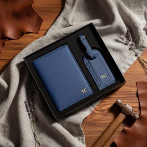 May include: A navy blue leather travel set, including a passport holder and luggage tag, presented in a black gift box. Both items are embossed with the gold initials "TC". The set is displayed on a wooden surface with leather accents.