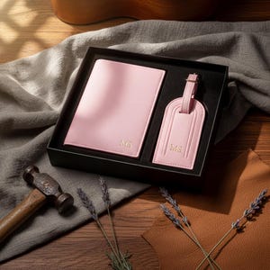 May include: A pink travel set in a black box, including a passport holder and luggage tag. Both items are embossed with the initials "MS". The set is presented on a wooden surface with a hammer and sprigs of lavender.