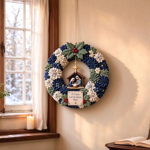May include: A circular fabric wreath featuring blue, white, and green folded fabric petals, accented with holly leaves and red berries. A central nativity scene sits below a gold star, with a sign below reading O Come Let Us Adore Him.