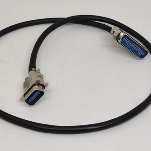 K&ouml;nnte beinhalten: Ein schwarzes Kabel mit zwei silbernen Steckern, jeweils mit blauem Innenraum. Das Kabel ist geschlungen, und die Stecker befinden sich an jedem Ende. Die Stecker haben ein D-f&ouml;rmiges Design.