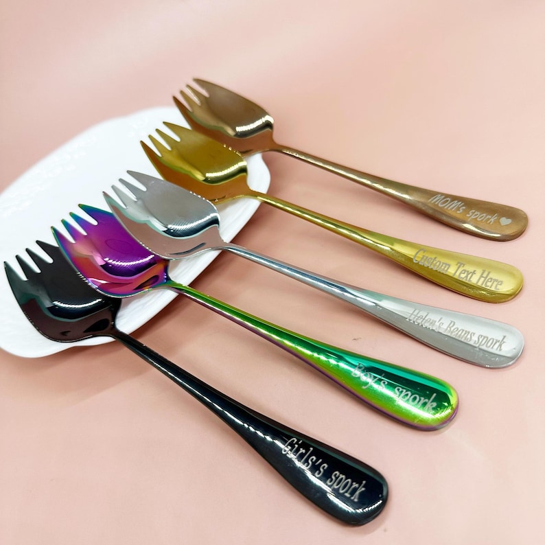 May include: A selection of sporks in gold, silver, and iridescent finishes. Each spork features a fork-like head and a long handle. The handles are engraved with text, including "Mom's spork" and "Girl's spork".