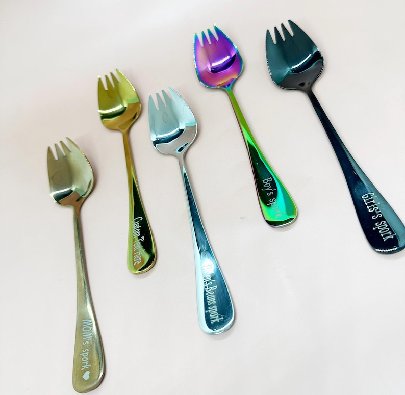 May include: Six metal forks with a distinctive three-pronged design. The forks display a range of colours, including gold, silver, and iridescent. Each fork has text engraved on the handle, such as "Mom's sport" and "Girls sport."