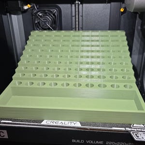 May include: A 3D printer is shown with a series of light green rectangular objects in the process of being printed. The objects have a series of oval cutouts. The printer is a Creality model with a build volume of 220x220x250mm.