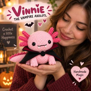 Può includere: Un peluche axolotl all'uncinetto rosa chiaro con occhi a bottone neri, due piccole zanne bianche e un mantello nero con fodera rossa. Il testo "VINNIE THE VAMPIRE AXOLOTL" appare sopra il giocattolo e "Handmade Magic" è in un cuore.