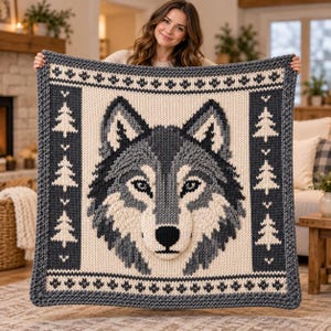 Pode incluir: Uma manta quadrada de malha com um grande gráfico central de uma cabeça de lobo em tons de carvão, cinza e creme. A borda apresenta um padrão repetitivo de pequenos pinheiros e formas geométricas, tudo feito com uma textura de lã grossa.