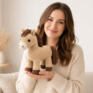 Könnte beinhalten: Ein gestricktes Spielzeugpferd in hellem Beige mit cremefarbenem Maul, dunkelbraunen Hufen sowie einer Mähne und einem Schweif aus dunkelbraunem Garn. Das Pferd hat schwarze Knopfaugen und eine durchgehend sichtbare Strickstruktur.