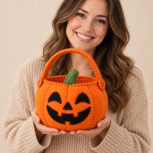 Può includere: Un cestino a forma di zucca in feltro arancione brillante con un volto di jack-o'-lantern nero cucito, occhi triangolari e una bocca frastagliata. Il cestino include un robusto manico arancione fissato con dettagli circolari e un gambo verde.