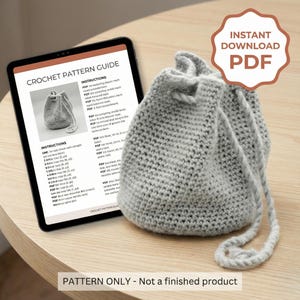 Könnte beinhalten: Ein hellgrauer gehäkelter Beutel mit Kordelzug neben einem Tablet, das eine Häkelanleitung anzeigt. Das Tablet zeigt Anweisungen und ein Bild der Tasche. Ein PDF-Download-Abzeichen ist sichtbar. Text unten: PATTERN ONLY - Not a finished product.