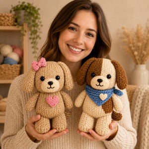 Puede incluir: Dos peluches de perro tejidos a ganchillo a mano. El perro de la izquierda es de color tostado claro con un lazo rosa en la oreja y un corazón rosa en el pecho. El de la derecha es tostado y marrón con un pañuelo azul y un corazón crema.