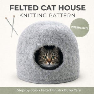May include: A gray felted cat house with a round opening, housing a tabby cat. The image includes knitting needles and text that reads "FELTED CAT HOUSE KNITTING PATTERN" and "INTERMEDIATE". The bottom text says "Step-by-Step • Felted Finish • Bulky Yarn".