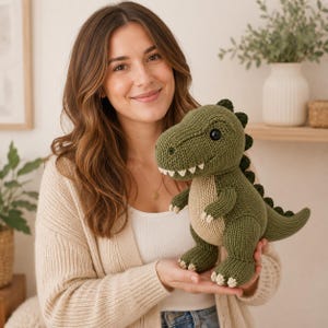 May include: A stuffed dinosaur toy crafted from olive green and cream-colored yarn. The plush features a textured knit surface, a row of dark green spikes along its back, small white claws on its feet and hands, and two round black plastic eyes.