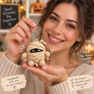 Puede incluir: Un llavero de momia tejido en crochet de color beige con un cuerpo redondeado envuelto en tiras de hilo, brazos y piernas pequeños. La momia tiene una máscara facial negra con dos ojos blancos curvados. Incluye una anilla y cadena plateada.