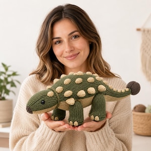 Puede incluir: Un juguete de dinosaurio anquilosaurio tejido con un cuerpo verde oscuro, vientre color canela y púas texturizadas de color beige claro a lo largo del lomo y la cola. El juguete tiene un hocico marrón oscuro, una maza caudal redondeada y ojos de cuentas negras.