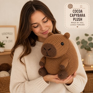 Pode incluir: Uma pelúcia de capivara tricotada em marrom com focinho e patas em marrom escuro, apresentando olhos de botão pretos. O texto na imagem diz: COCOA CAPYBARA PLUSH, MADE BY YOU, LOVED FOREVER. A pelúcia tem um corpo arredondado e orelhas pequenas.