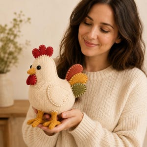 Peut inclure: Un jouet en peluche tricoté en forme de poulet couleur crème avec une crête et des barbillons rouge vif, un bec jaune et des pattes orange. La queue se compose de trois plumes arrondies superposées en rouille, jaune doré et vert olive.
