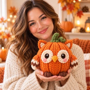 May include: A round, orange crocheted pumpkin-shaped owl plush toy. The owl features a green stem on top, large white eyes with black pupils, pink cheeks, a small yellow beak, and brown feet. The wings are striped with white, orange, and brown.