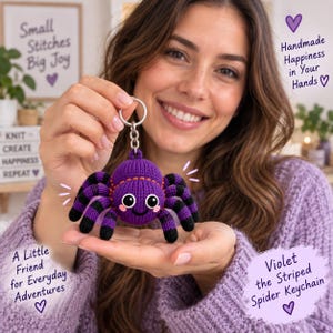 Puede incluir: Un llavero de araña de ganchillo a rayas moradas y negras con ojos blancos grandes, mejillas rosadas y una pequeña sonrisa. La araña está unida a una anilla y cadena de metal plateado. El texto en la imagen dice: Small Stitches Big Joy, Handmade Happiness in Your Hands, A Little Friend for Everyday Adventures y Violet the Striped Spider Keychain.