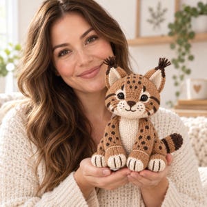 Op de afbeelding: Een gebreide lynx knuffel met een beige lichaam met donkerbruine vlekken, een crèmekleurige borst en snuit, zwart getipte oren met pluimpjes en een korte, gestreepte staart. Het knuffeldier heeft grote zwarte ogen en een geborduurde snuit.