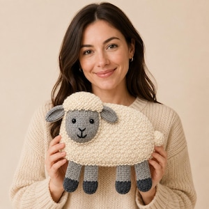 May include: A knitted sheep toy featuring a cream-coloured textured body, a grey face with black button eyes, and a stitched black mouth. The sheep has grey ears and four grey legs with darker grey hooves at the bottom, crafted from woollen yarn.