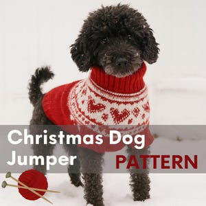 Puede incluir: Un perro negro con un jersey navideño rojo y blanco estampado, de pie en la nieve. El jersey tiene un cuello alto y un diseño festivo. La imagen también incluye una madeja de lana roja y agujas de tejer.