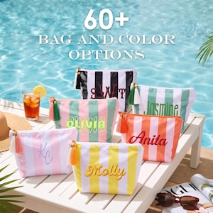 May include: A collection of five rectangular zippered pouches featuring vertical stripes in various colors including black, white, pink, green, orange, and yellow. Each pouch is personalized with embroidered names and includes a decorative tassel.