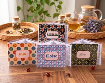 May include: Four triangular tabletop game screens with clear plastic covers, each featuring a unique pattern and a personalized name label: AMELIA, IRIS, Eloise, and Lena. The screens display internal score tracking charts and are accompanied by small red dice.