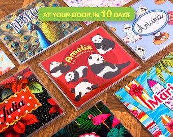 May include: A collection of rectangular personalized plastic name tags featuring various graphic designs including a peacock, pandas with the name Amelia, dogs, surfboards with the name Maria, and poinsettias with the name Julia.