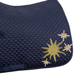 May include: A navy blue quilted saddle pad with a diamond pattern. The pad features an embroidered design of a yellow sun and three gold stars on the lower right corner. It has navy blue straps for securing it to the saddle.