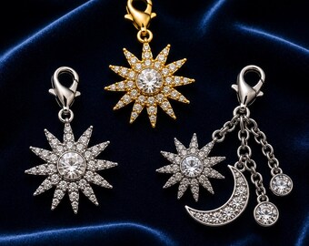 May include: Three charm pendants with a celestial theme. One is gold-toned with a sunburst design and a central clear stone. The other two are silver-toned, one with a sunburst and the other with a crescent moon and dangling clear stones.