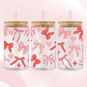 Könnte beinhalten: Drei Glasbecher mit Bambusdeckeln und Strohhalmen. Die Becher sind mit einem Muster aus rosa und roten Schleifen, Herzen und Sternen verziert. Der Hintergrund ist ein zartes Rosa.